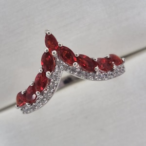 May include: A silver ring with a V-shaped design set with red and white gemstones.