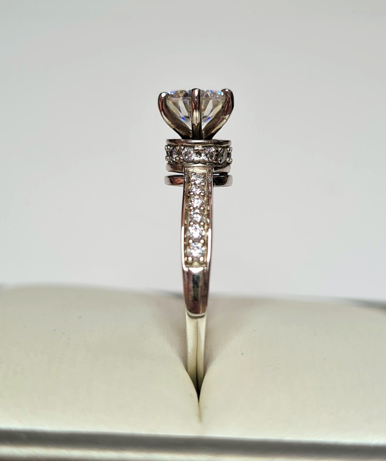 May include: A silver ring featuring a large, clear, round diamond set in a flower-shaped setting. The band is also set with smaller diamonds.