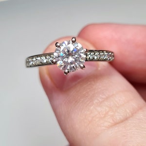 May include: A silver engagement ring with a large, round, clear centre stone and a band of smaller, clear stones.