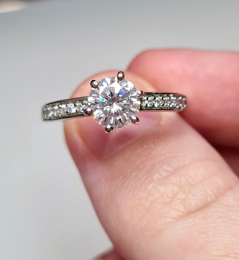 May include: A silver engagement ring with a large, round, clear centre stone and a band of smaller, clear stones.