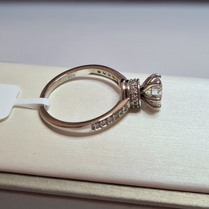 May include: A silver ring with a large, clear centre stone and smaller stones set in a band around the centre stone. The ring is marked "925" on the inside of the band.