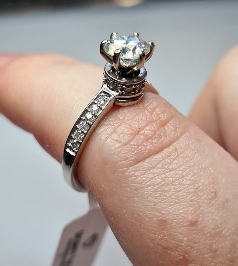 May include: A silver ring featuring a large, clear, round gemstone set in a crown-like design. The band is embellished with smaller, clear gemstones.