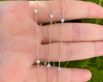 May include: Three delicate gold chains with small, clear gemstones. The chains are layered on top of each other and are held in a hand.