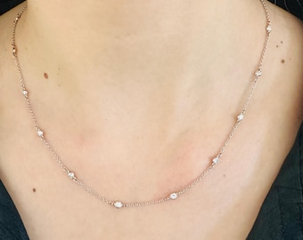 May include: Delicate rose gold necklace featuring multiple small, round, clear gemstones evenly spaced along the chain. The necklace is displayed against a neutral background, highlighting the sparkle of the gemstones. A simple and elegant piece of jewelry.