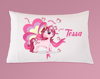 May include: A white pillowcase with a pink unicorn with a rainbow mane and tail. The unicorn has a pink bow in its hair and is surrounded by pink hearts and ribbons. The text "Tessa" is printed on the pillowcase.