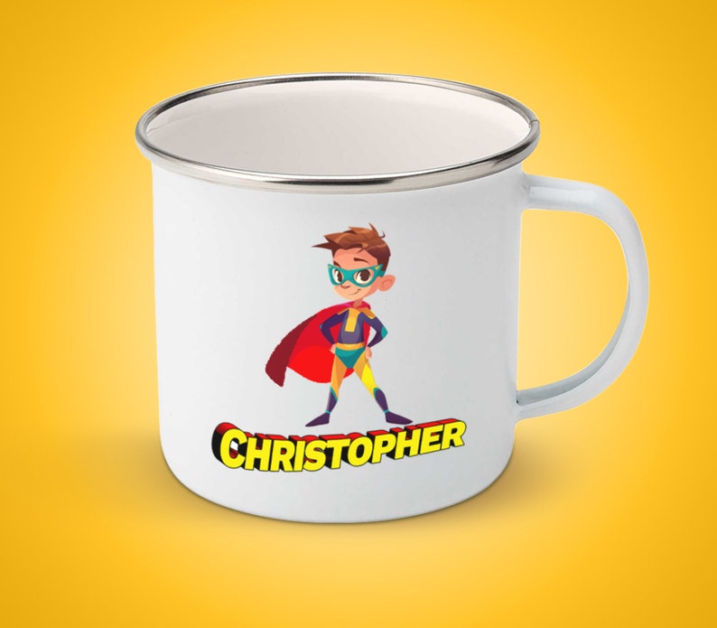 Op de afbeelding: Witte emaille mok met een cartoonillustratie van een superheldenjongen die een rode cape, een geel en blauw pak en een groene bril draagt. De tekst "CHRISTOPHER" is in gele letters onder de illustratie gedrukt.