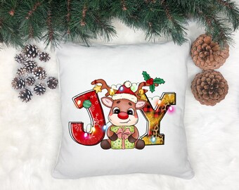May include: White pillow with a red, gold, and black design featuring a cartoon reindeer holding a gift box. The design says "JOY" with lights around the letters.