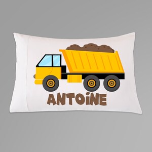 May include: A white pillowcase featuring a yellow dumper truck carrying brown dirt. The truck has a brown cab and black wheels. The name "ANTOINE" is printed in brown below the truck.