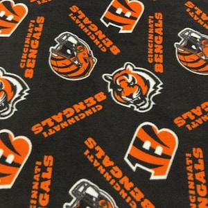 Könnte beinhalten: Schwarzer Stoff mit einem sich wiederholenden Muster aus orangefarbenen und weißen Cincinnati Bengals-Logos. Die Logos beinhalten den Teamnamen, einen Tigerkopf und einen Footballhelm.