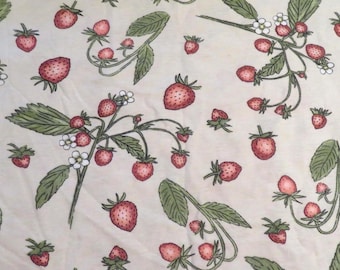 May include: A cream-coloured fabric featuring a repeating pattern of strawberries and leaves. The strawberries are red with green stems, and the leaves are green. Small white flowers are also present in the design.