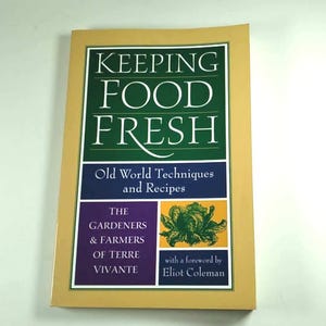 Pode incluir: Um livro intitulado "KEEPING FOOD FRESH" com o subtítulo "Old World Techniques and Recipes". A capa apresenta um design verde e branco com texto e uma borda amarela. O livro está sobre uma superfície branca.
