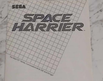 May include: A black and white box cover for the video game Space Harrier. The cover features the game's title in a bold, white font. The text "For Atari ST Series, Commodore 64 & 128 and Amiga" is printed in smaller, grey font at the bottom of the cover. The cover also includes a description of the game: "Blast incredibly evil, alien invaders into oblivion. Dodge deadly obstacles. And restore peace to the beautiful Land of Dragons."