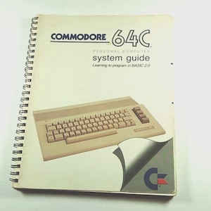 May include: A spiral-bound Commodore 64C system guide. The cover features the Commodore 64C logo, the words "system guide", and an illustration of the computer's keyboard. The guide is designed to teach programming in BASIC 2.0.