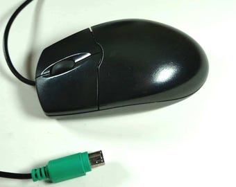 Könnte beinhalten: Eine schwarze Computermaus mit einem Scrollrad und einem grünen Stecker. Die Maus hat eine glänzende Oberfläche und ein schwarzes Kabel. Die Maus liegt auf einer weißen Oberfläche.