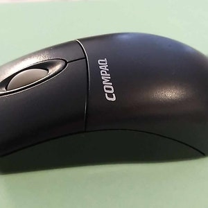 May include: A black wired computer mouse with a single button and a scroll wheel. The mouse has the word "COMPAQ" printed on the top.