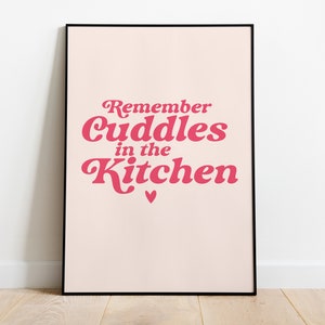 Op de afbeelding: Een roze en witte printbare wandkunstprint met de tekst "Remember Cuddles in the Kitchen" in een retro fontstijl.