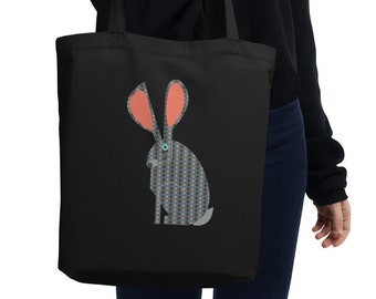May include: Black tote bag with a geometric patterned rabbit design. The rabbit has blue eyes and pink ears.