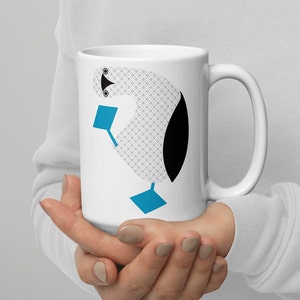 May include: White ceramic mug with a blue-footed booby illustration. The bird is depicted in a stylized, geometric design with a gray and white patterned body, black head, and blue feet.
