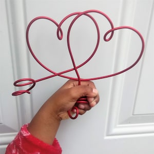 May include: A red metal sculpture of two intertwined hearts with a curled arrow at the bottom.