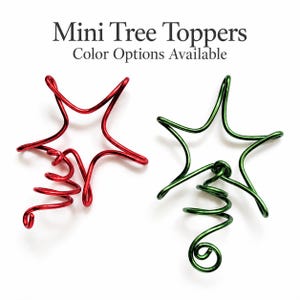 Könnte beinhalten: Zwei Mini-Baumspitzen in Sternform, eine in Rot und eine in Grün, gefertigt aus durchgehendem Draht mit einer spiralförmigen Basis. Der Text "Mini Tree Toppers" und "Color Options Available" steht über den beiden Drahtsternen.