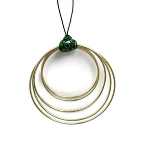 Peut inclure: Une décoration en métal doré avec quatre cercles concentriques, suspendue à une boucle de fil vert.