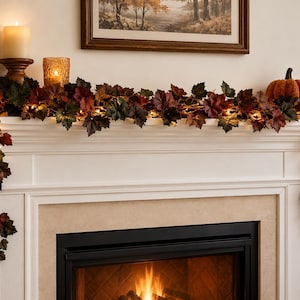 May include: A decorative garland featuring artificial autumn leaves in shades of red, orange, and brown, intertwined with small warm white string lights. The garland is draped across a white fireplace mantel, with ends hanging down on both sides.
