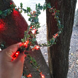 Op de afbeelding: Rode LED-lampjes die aan een groene krans van kunstmatige klimop zijn geregen, gewikkeld rond twee boomstammen.