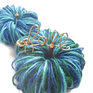 May include: Two blue and green yarn pumpkins with a gold wire "fall" sign.