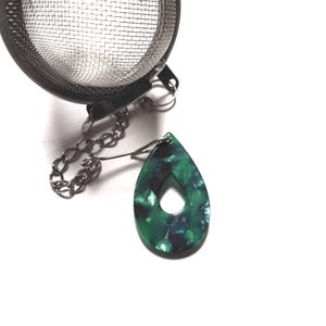 Może przedstawiać: Stalowy zaparzacz do herbaty z łańcuszkiem i zielonym i czarnym marmurowym uchwytem na torebkę herbaty.