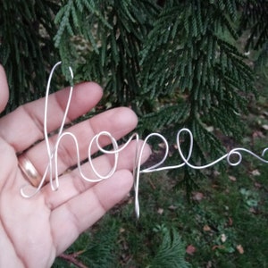 May include: A silver wire sculpture of the word "hope" held in a hand.