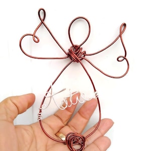 May include: A copper wire angel ornament with the name "Katie" written in white wire.