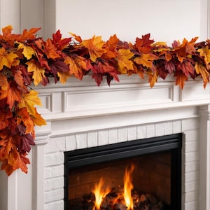 May include: A decorative garland featuring a dense arrangement of artificial maple leaves in vibrant shades of red, orange, yellow, and deep burgundy. The foliage is layered to create a full, textured appearance, draped across the top of a fireplace.