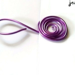 Puede incluir: Un alambre morado está doblado en forma de lágrima a la izquierda y en espiral a la derecha.