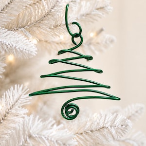 Peut inclure: Une décoration en fil métallique vert foncé en forme de sapin de Noël stylisé. L'ornement est fabriqué à partir d'une seule pièce de fil métallique continu, présentant une spirale à la base et une boucle au sommet pour la suspension.