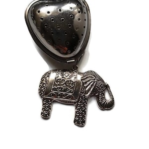 May include: Silver tea infuser shaped like a heart with a silver elephant attached to the bottom. The elephant has an ornate design.