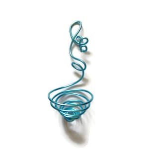 Op de afbeelding: Een blauwe metalen draadskulptuur in de vorm van een bloem met een spiraalvormige basis.