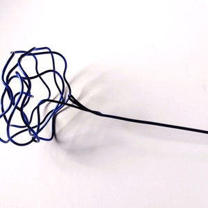 Può includere: Una scultura di filo di ferro blu a forma di fiore con un gambo lungo e sottile.