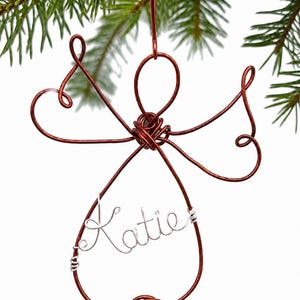 Peut inclure: Une décoration en fil de fer de couleur cuivre en forme d'ange avec un corps en forme de goutte et des ailes. Le prénom Katie est écrit en fil de fer de couleur argentée au centre du corps. L'ornement possède une boucle pour le suspendre.