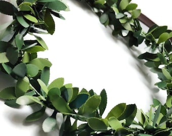 May include: A green leaf wreath with a brown ribbon tied around it. The wreath is made of artificial leaves and is perfect for decorating a home or adding a touch of greenery to a special occasion.