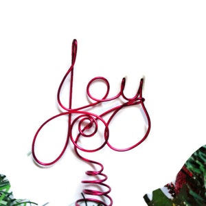 Puede incluir: Adorno para la cima del árbol de Navidad de alambre rojo con forma de la palabra "Alegría".