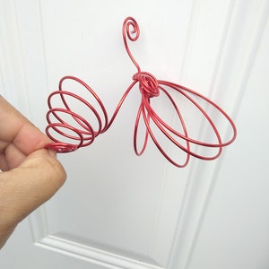 Może przedstawiać: Rzeźba motyla z czerwonego drutu metalowego o spiralnym wzorze. Rzeźba wykonana jest z cienkiego drutu i ma około 25 cm długości.