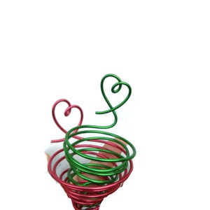Könnte beinhalten: Eine rote und grüne Drahtskulptur in Form eines Herzens. Der Draht ist zu einer Spirale gedreht.