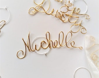 May include: Gold wire wine glass charms with names written on them. The names are Michelle, Denise, Ken, and Cameron.