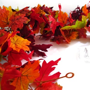 May include: A garland of artificial autumn leaves in shades of red, orange, yellow, and burgundy. The leaves are arranged in a cascading pattern, creating a festive and autumnal display.