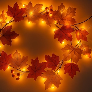 May include: A fall-themed LED light string featuring maple leaf decorations in shades of red, orange, and yellow. The battery-operated lights are strung together with small berries and a clear battery pack.