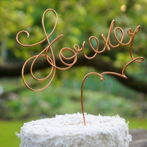 May include: A white cake with a copper wire topper that says "Lovely" in cursive.