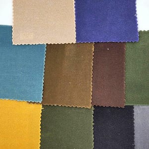 Può includere: Una collezione di campioni di tessuto in vari colori, tra cui beige, blu, verde acqua, marrone, verde oliva, giallo, nero e grigio. Ogni campione ha un aspetto strutturato e un bordo frastagliato, che mostra le diverse opzioni di materiali.