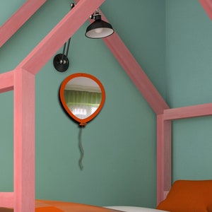 May include: A child's bedroom with a pink house-shaped bed frame and an orange bedspread. A balloon-shaped mirror hangs on the teal wall. A black lamp is mounted above the bed. The room has a white desk and chair.
