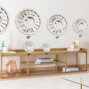 May include: A set of six white, decorative, round mirrors with a sunburst design. The mirrors are arranged in a row on a gold metal shelf with two shelves. The mirrors are 24 inches, 20 inches, 16 inches, 12 inches, 10 inches, and 8 inches in diameter.