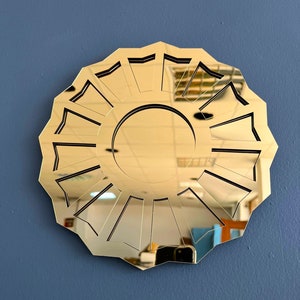 May include: A gold-colored, round mirror with a geometric design. The mirror has a sunburst pattern with 12 points.